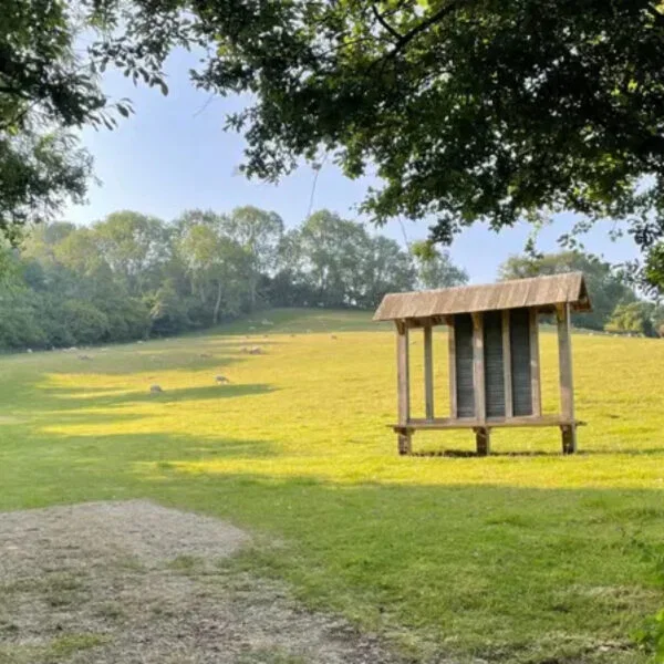Open houten schuilhut met gedenkplaten aan de rand van een weide